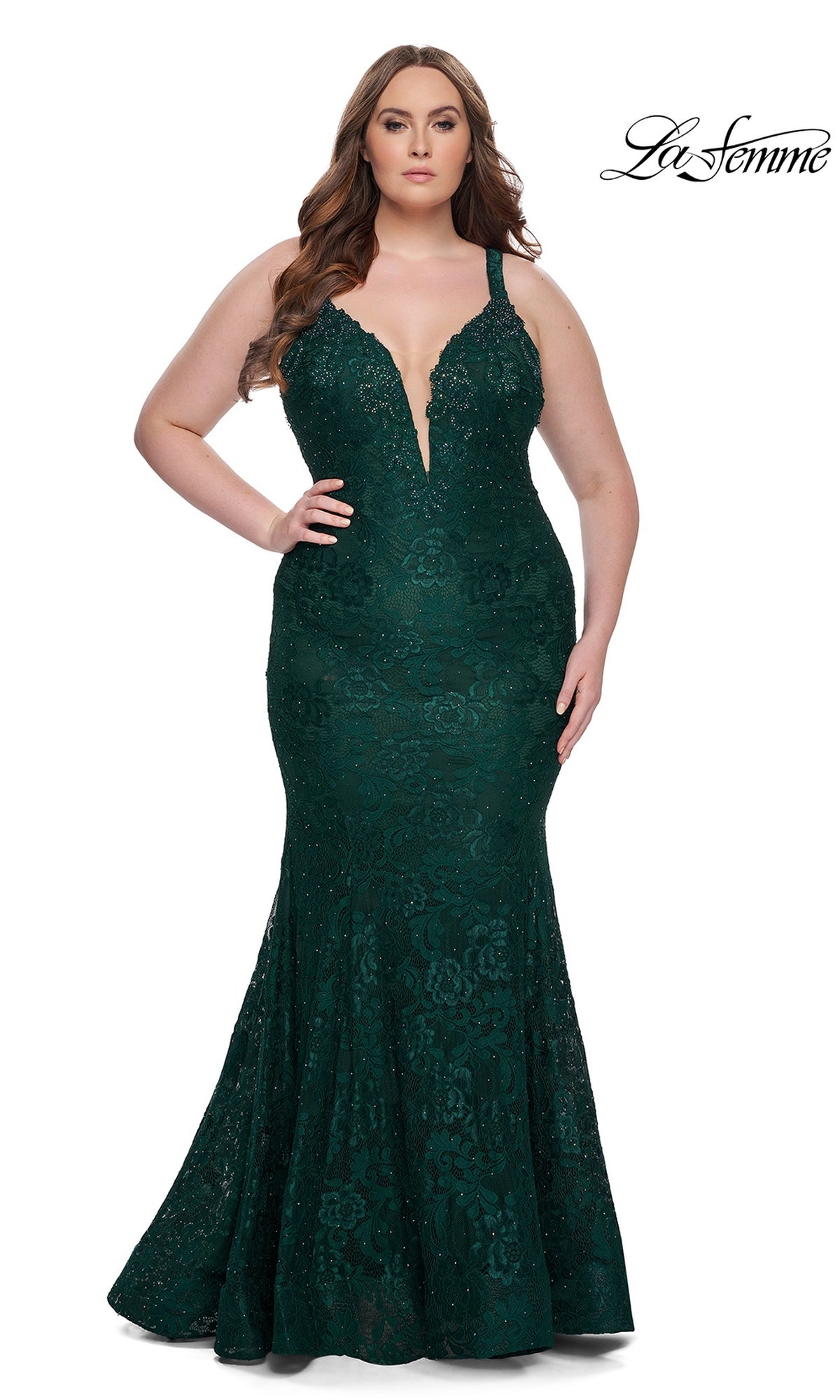 A woman in the La Femme Long Prom Dress 29052, featuring dark emerald floral lace, a plunging neckline, and thin straps, stands against a white background. The La Femme logo is shown in the top right corner.